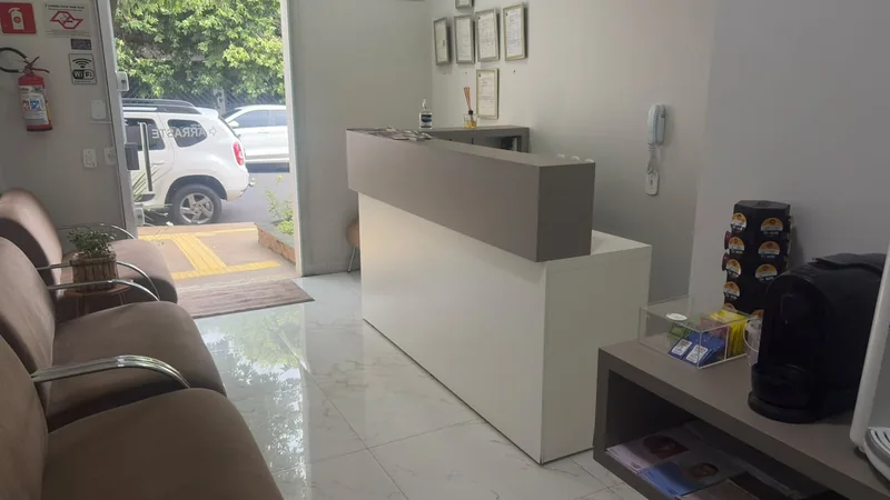Recepção do consultório, com balcão branco, cadeiras e entrada envidraçada
